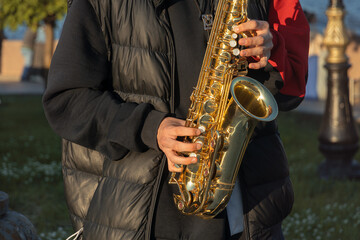 Obraz premium Unrecognizable street musician playing golden alto saxophone close up