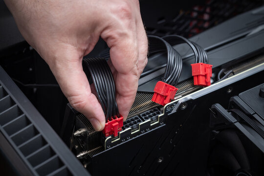 Close up of a hand connecting red modular PCI power connectors to a powerful graphics card inside a PC case. Building or upgrading a powerful gaming PC