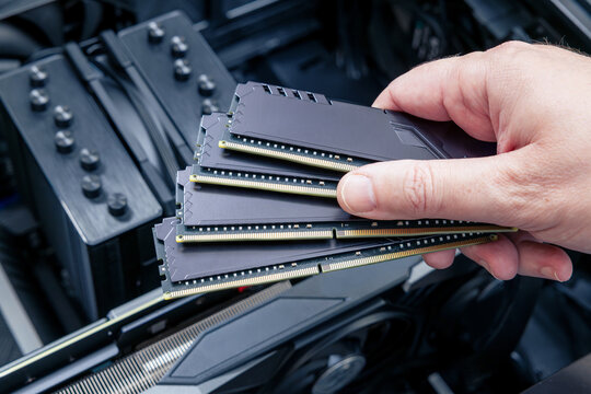 Technician holds expensive DDR memory modules fanned over an open PC, with cooling equipment and graphics card visible
