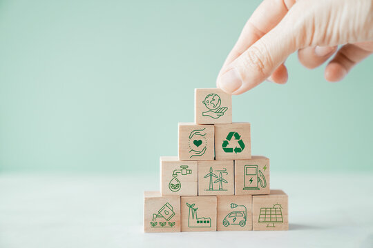 Hands holding wooden blocks with green sustainable environmental icons, renewable energy concept
