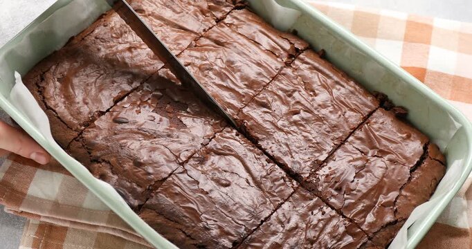 Woman cutting yummy chocolate brownie in baking dish at table, closeup