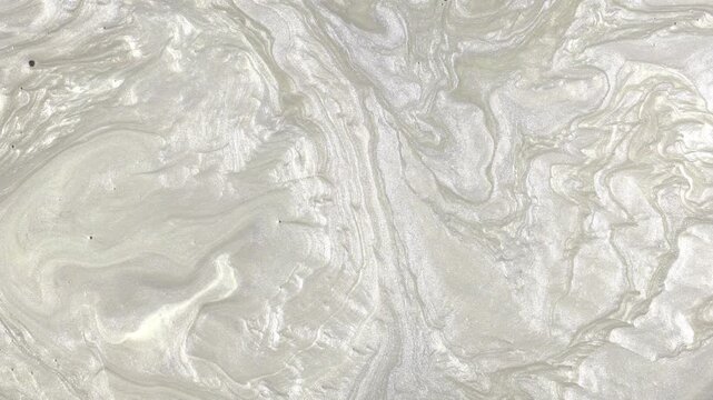 A flow of silvery and pearlescent white liquid with an elegant metallic sheen. The slow movement of these swirling paints or fluids creates a luxurious, smooth, and captivating liquid-marble texture.