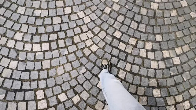 First-person walking view over patterned cobblestone pavement in Ljubljana old town, showing shoes, curved stone design and urban travel texture.