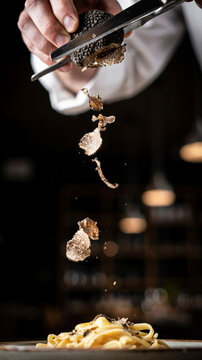 Black truffle being shaved over pasta dish in upscale restaurant setting