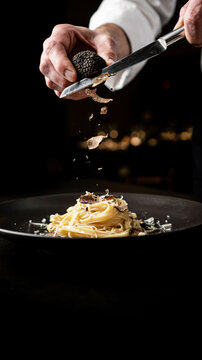 Chef grating black truffle over pasta dish on dark restaurant table
