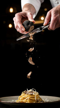 Chef grating black truffle over pasta dish in elegant restaurant setting