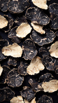Black and white truffle slices arranged on a dark surface for culinary presentation