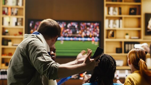 Tight framing shows football supporter at home on couch holding smartphone while watching match on television, feeling upset after seeing negative online match results during tense live game action.