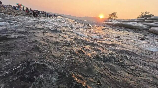 Close-up shot of fast-flowing rocky river water originating from mountain springs during a bright sunset in Sylhet, Bangladesh. Highlighting the rapid current, sparkling water ripples, and golden hour