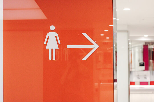 Modern female restroom direction sign with orange wayfinding symbol