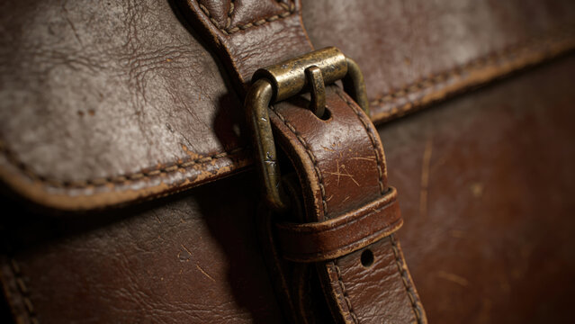Close-up of vintage brown leather satchel strap with brass buckle, rustic texture
