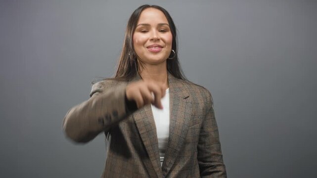 Woman pointing fist forward with outstretched hand and smiling face, wearing plaid blazer and hoop earring in studio; confidence empowerment.