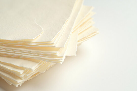 Close up of torn edges of stacked off-white handmade paper sheets with rough texture isolated on white background for crafts