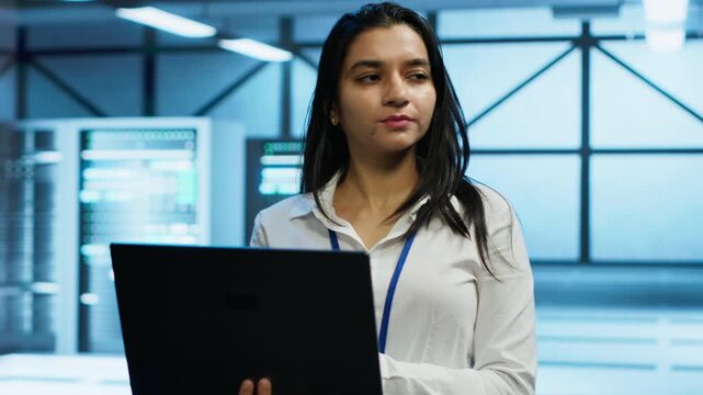 Woman system administrator monitors cybersecurity risks inside a data center with a laptop, connecting network security and data protection with enterprise infrastructure work