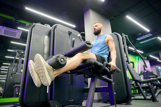 Muscular man with a beard trains his legs using gym equipment to build lower body strength in a contemporary fitness center during the day