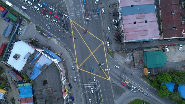 Aerial view of traffic moving through a busy city intersection with yellow box markings on the asphalt surface during daytime.