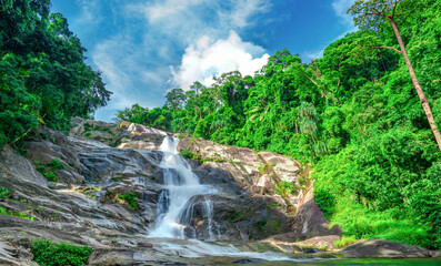Beautiful tropical waterfall cascading over granite mountain rocks beneath blue sky. Lush rainforest in Thailand. Wilderness landscape for travel and nature theme. Ecotourism and conservation. © Fahroni
