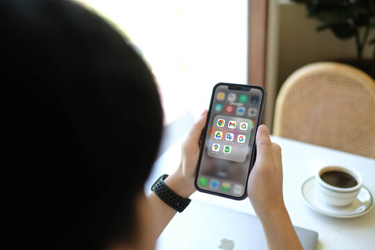 Bangkok, Thailand. July 27, 2026; An over the shoulder view of a person holding a smartphone displaying a Google applications folder filled with recognizable brand icons next to a coffee cup.