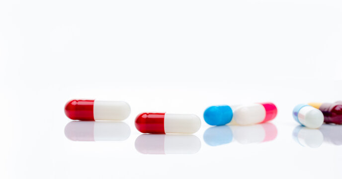 Red-white antibiotic capsule pill on blur multi-colored capsules background. Antibiotic drug resistance concept. Pharmacy horizontal banner. Prescription drugs. Pharmaceutical industry. Healthcare.