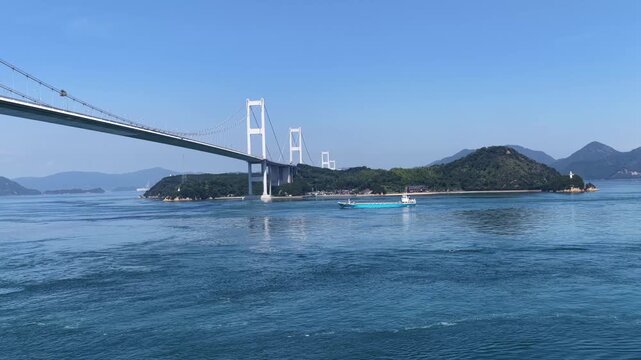 Low aerial view of Kurushima Kaikyo Bridge with tidal currents and passing ship in Japan