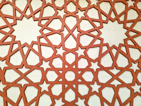 Islamic geometric wall ornament pattern background. Terracotta brown star shape decoration on white wall surface.