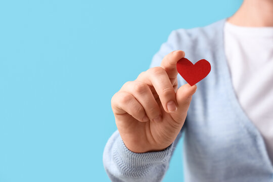 Person holding a small red paper heart, expressing love, care, and generosity on a blue background