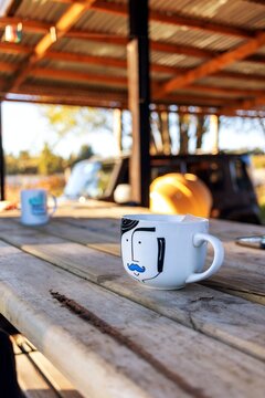 Outdoor coffee break with illustrated mugs on a rustic wooden table under a porch