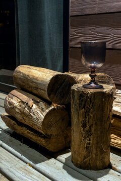 A glass goblet sitting on a wooden log next to firewood on a cottage porch at night