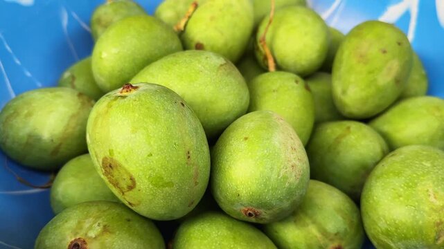 Fresh green raw mangoes piled inside blue bowl for culinary preparation.