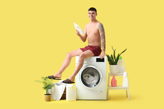Young man in underpants with detergent doing laundry on yellow background