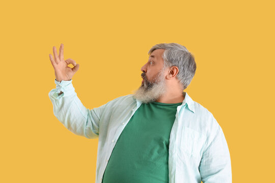 Shocked mature bearded man showing OK on yellow background
