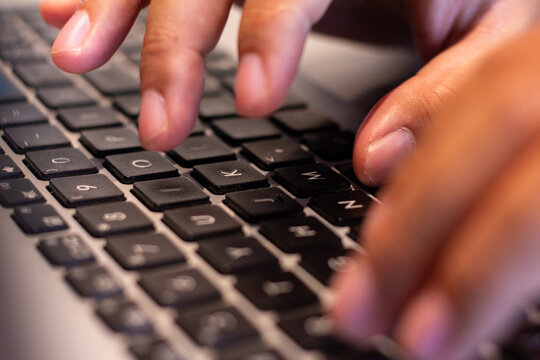 Person typing on a laptop keyboard with fingers close up