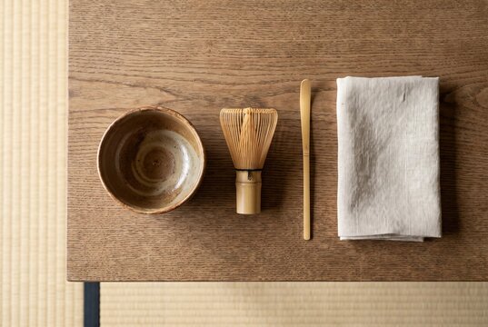 木の台に並べられた茶碗、茶筅、茶杓、布巾。畳の背景と自然光が、茶道の静けさと丁寧な所作を美しく伝える一枚