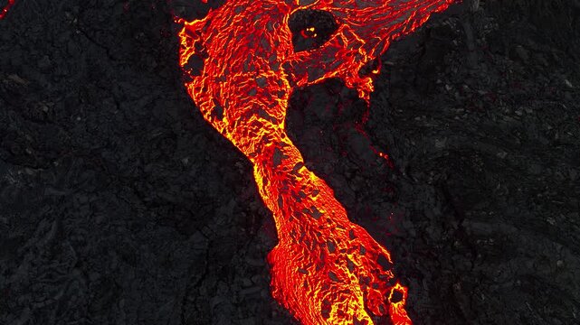 Molten lava river flowing through dark volcanic rock landscape