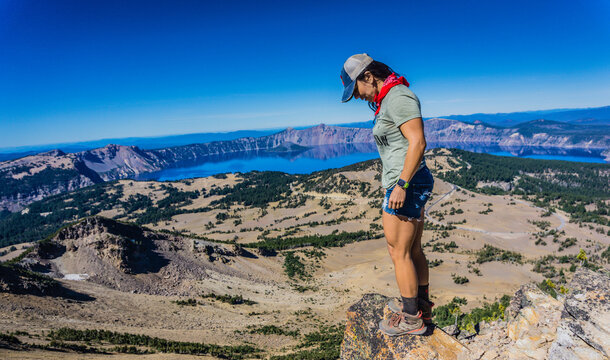 Hiker stands atop volcanic peak, gazing at Crater Lake