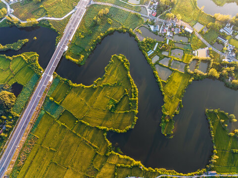 A high-angle aerial shot of a winding river, adjacent fields, roads and small settlements in rural landscape.