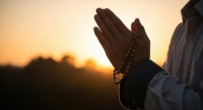 Person holding wooden prayer beads with hands together in prayer at a beautiful golden sunset