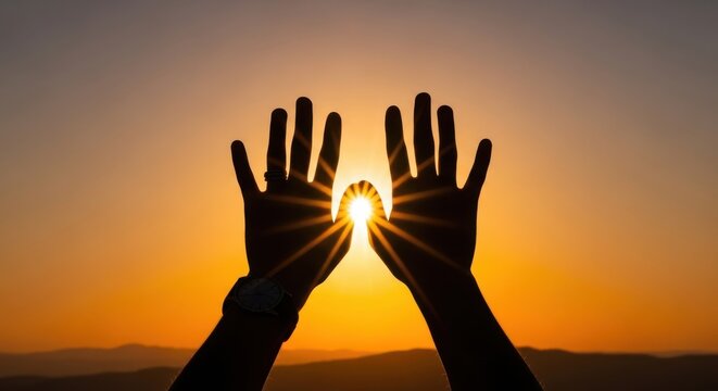 Silhouette of two hands reaching up towards the bright sun during a golden sunset