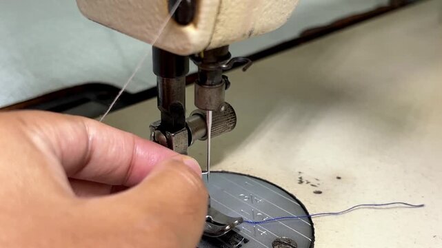 Close up of a female seamstress threading a needle on an industrial high-speed sewing machine