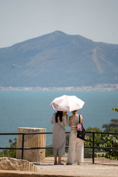 Two women with white umbrellas in the ancient ruins of Carthage, on the outskirts of Tunis, Tunisia, with Lake of Tunis in the background
