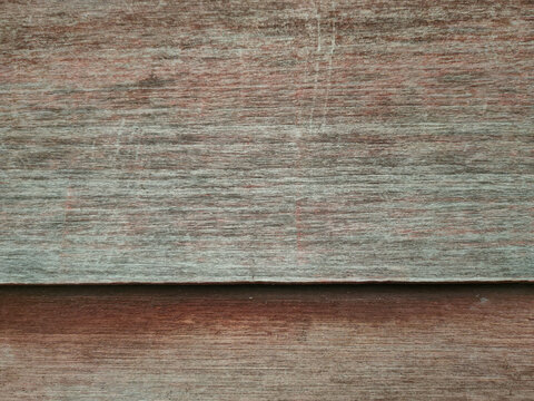 A close-up of two overlapping weathered wooden boards showing horizontal grain and subtle reddish tones