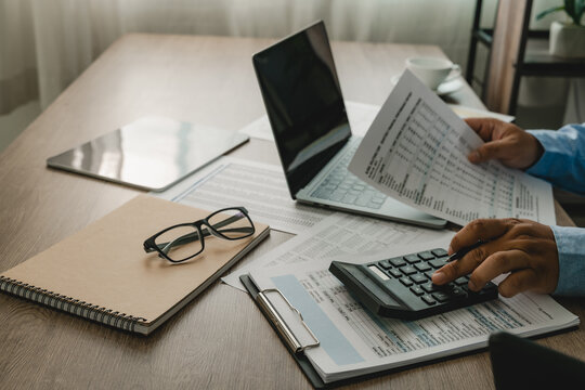 Business professional use a calculator while reviewing printed accounting reports on a wooden desk a laptop, supporting financial calculation, report checking, business expense documentation.