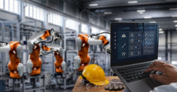 Engineer wearing hard hat and safety glasses uses laptop checklist dashboard in robotic factory, reviewing inspection, safety compliance, quality control, manufacturing verification process.