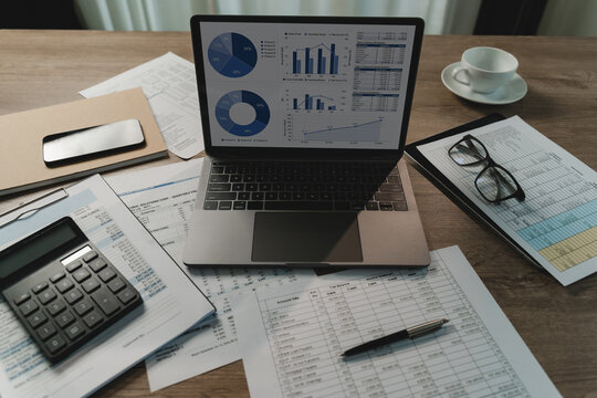 Laptop displays charts and financial tables beside a calculator, documents, smartphone, and pen on a desk, supporting financial analysis, budgeting, accounting, and management reporting.