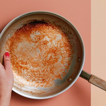 Dirty stainless steel frying pan with burnt grease stains held by a hand on a colorful backdrop, perfect for kitchen cleaning and chore concepts