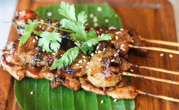 Closeup view of grilled pork belly skewers served on a banana leaf atop a wooden board.