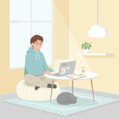 Fototapeta premium A man wearing glasses sits on a bean bag chair while working on his laptop at a low table in a cozy room with his sleeping cat nearby.