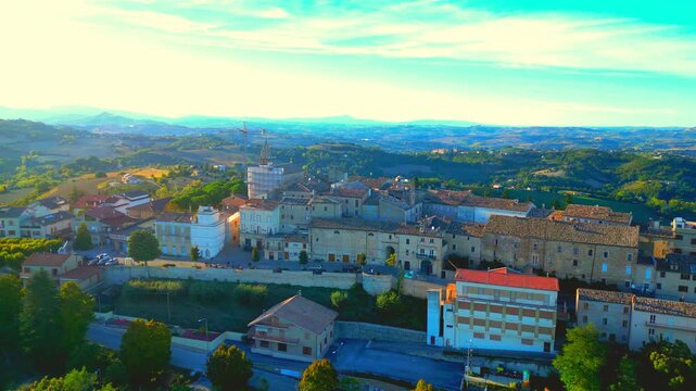 Sublime aerial pullback pedestal up shot from Monte Rinaldo, the town center and its buildings coming into full view, surrounded by sumptuous Marche hillscapes, blue ridges in the background, clouds