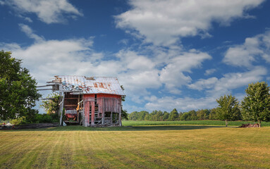 Old, abandoned red barn in a rural landscape against cloudy sky © Balint Radu