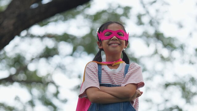 Active Asian little kids pretending to be superheroes playing together outdoors in nature park. Children roleplay, imaginative fantasy, and brave hero childhood lifestyle.
